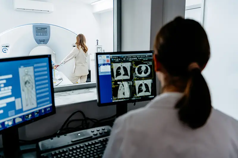 CT scan room with imaging monitors and a patient being prepared for preventive CT imaging.