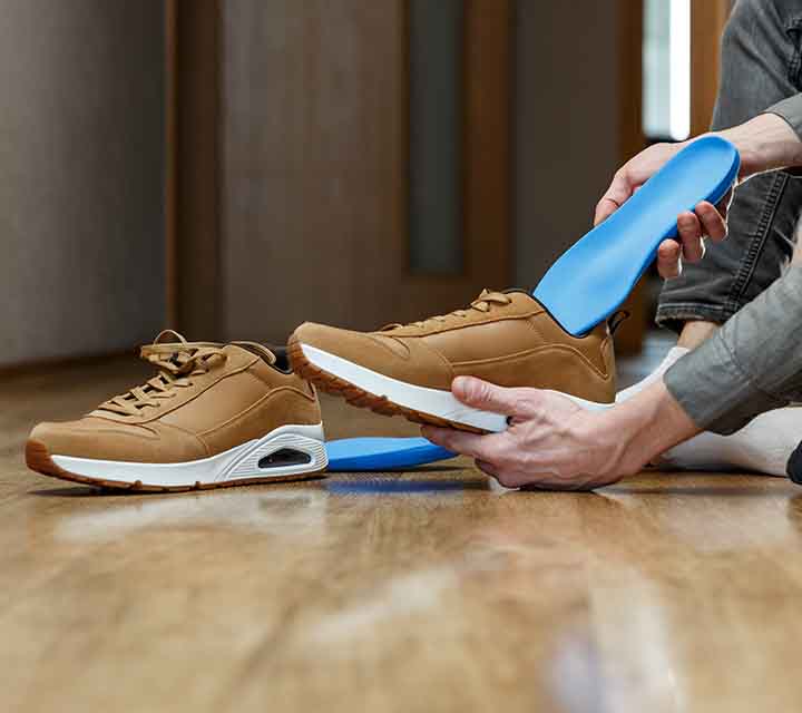 Blue custom orthotic insoles being placed into brown casual shoes.