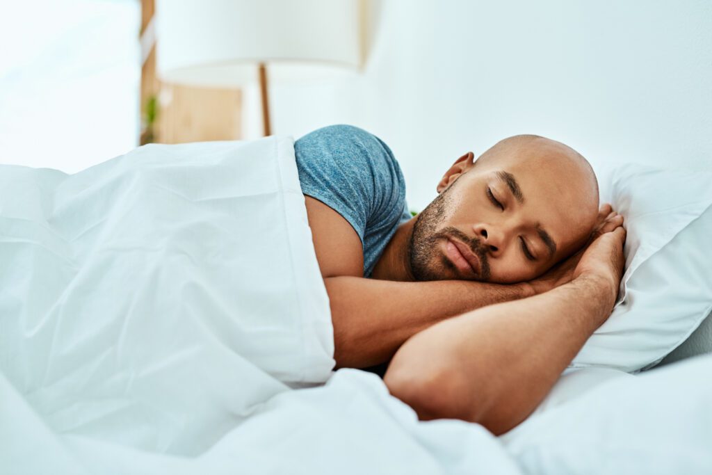 A man sleeps on a comfortable stack of pillows under crisp white blankets, showing the importance of healthy sleep habits.