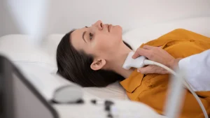 Patient receiving a thyroid ultrasound with a handheld transducer positioned at the front of the neck.